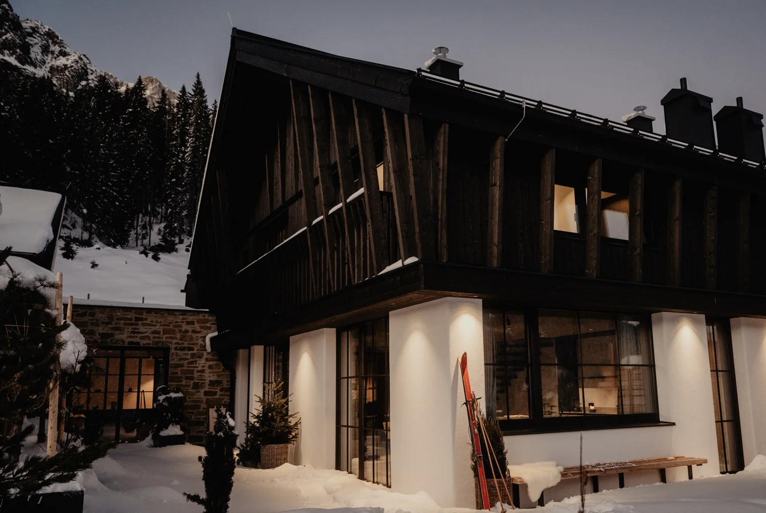 Beleuchtete Birgkar-Lodge in der Dämmerung, schwarze Holzfassade im Schnee